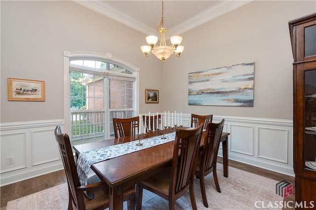 dining space with crown molding, wood finished floors, a wainscoted wall, a notable chandelier, and a decorative wall