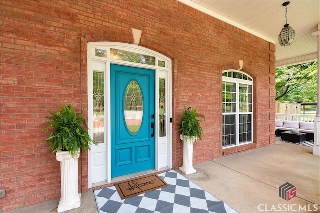 entrance to property with covered porch, brick siding, and an outdoor living space