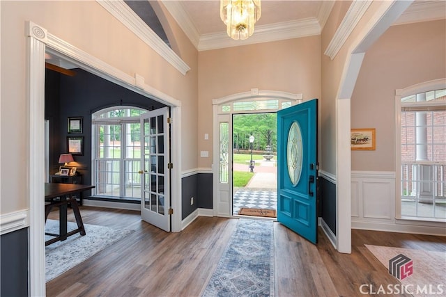 foyer entrance with ornamental molding, wainscoting, wood finished floors, and a chandelier