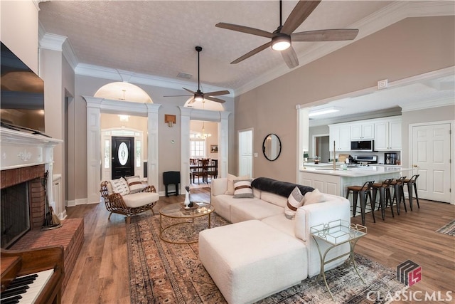 living area with arched walkways, a fireplace, wood finished floors, ceiling fan with notable chandelier, and ornamental molding