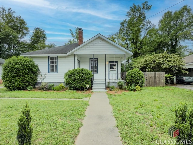 bungalow with fence, covered porch, a chimney, and a front yard