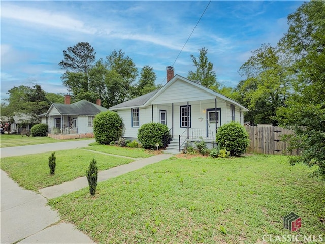 bungalow-style home with a porch, a front lawn, fence, and a chimney