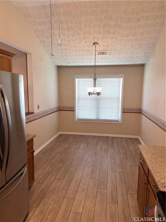 unfurnished dining area featuring light wood-style floors, baseboards, a notable chandelier, and visible vents