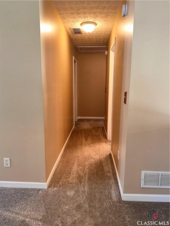 corridor with carpet floors, baseboards, visible vents, and attic access