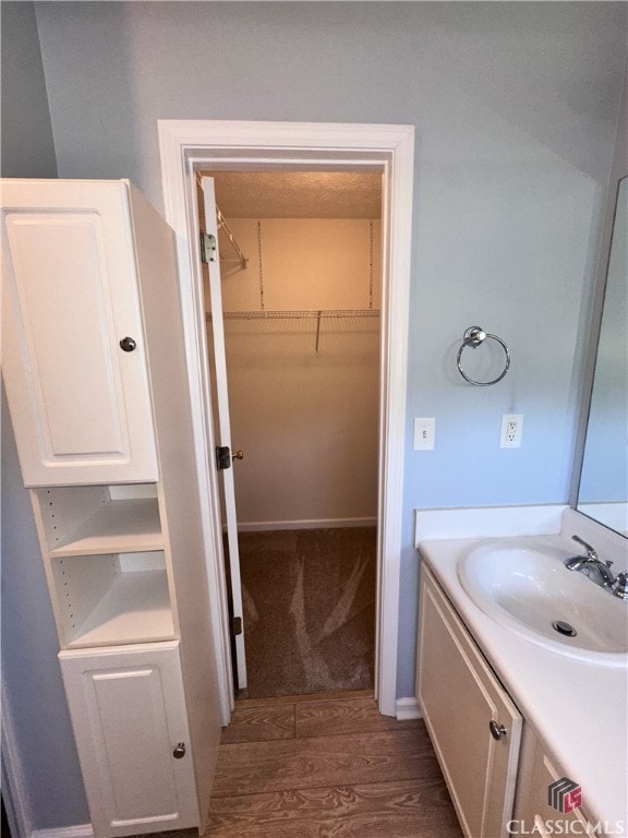 bathroom with vanity, wood finished floors, and a walk in closet