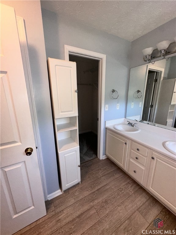 full bath with double vanity, a textured ceiling, a sink, and wood finished floors