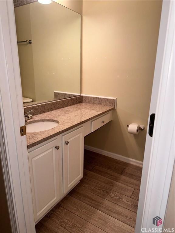 half bath featuring toilet, baseboards, wood finished floors, and vanity