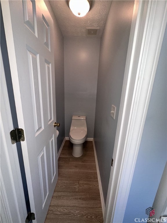 bathroom with toilet, a textured ceiling, baseboards, wood finished floors, and visible vents