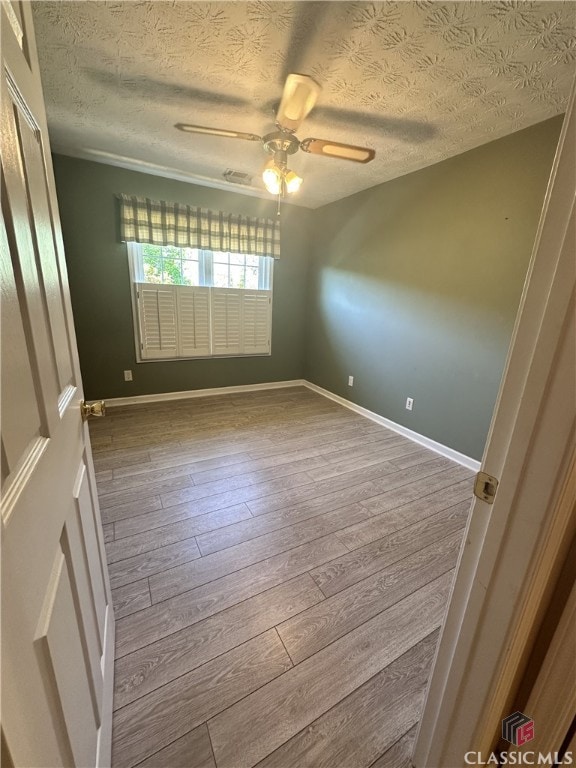spare room featuring a textured ceiling, a ceiling fan, baseboards, visible vents, and hardwood / wood-style flooring