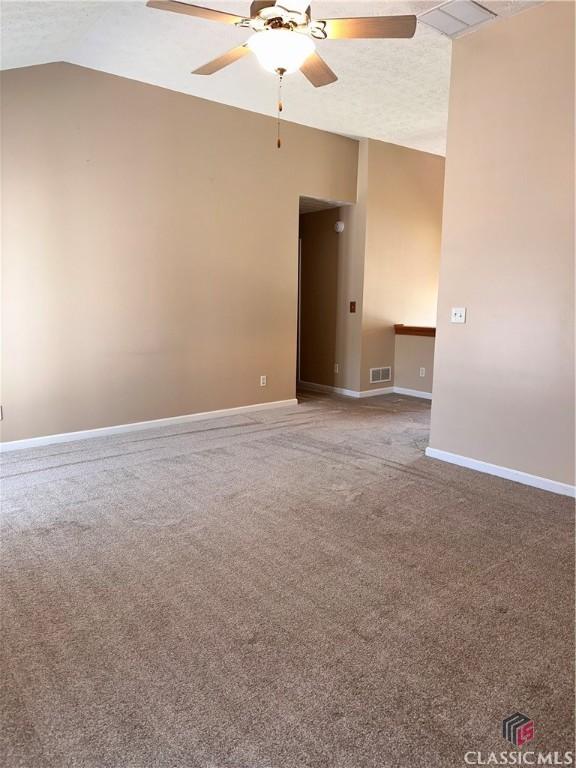 empty room with a ceiling fan, visible vents, carpet floors, baseboards, and lofted ceiling