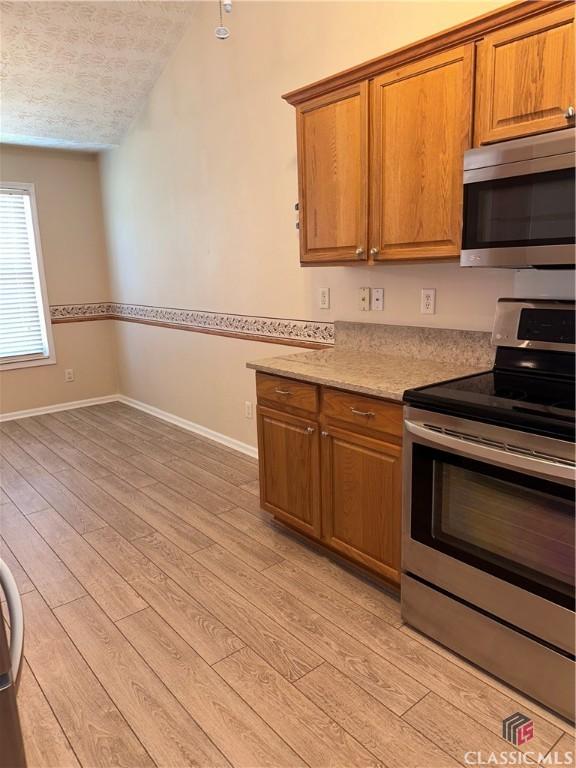 kitchen featuring brown cabinets, baseboards, stainless steel appliances, and light wood-type flooring