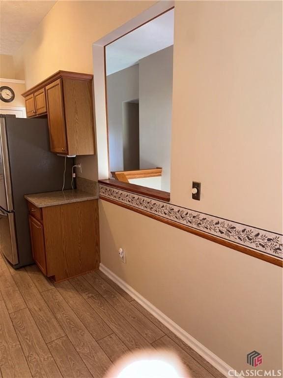 kitchen with light wood-type flooring, brown cabinetry, freestanding refrigerator, and light countertops