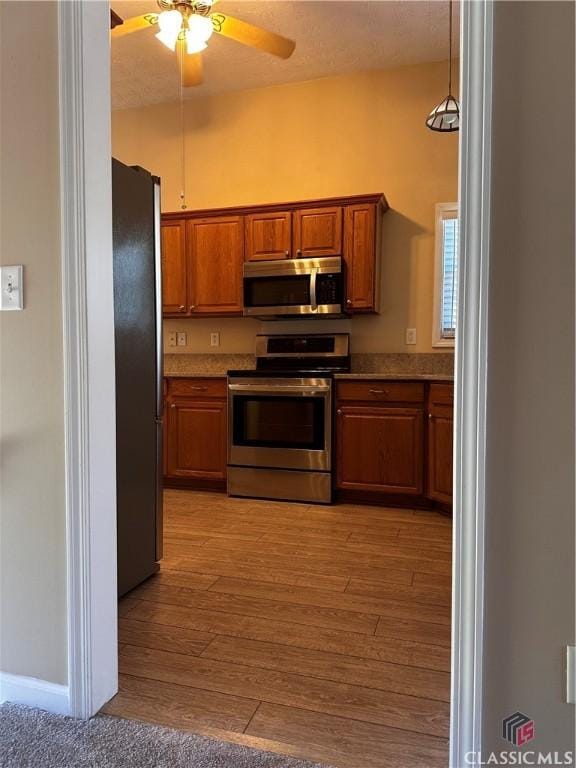 kitchen featuring ceiling fan, appliances with stainless steel finishes, hanging light fixtures, light wood-type flooring, and brown cabinets