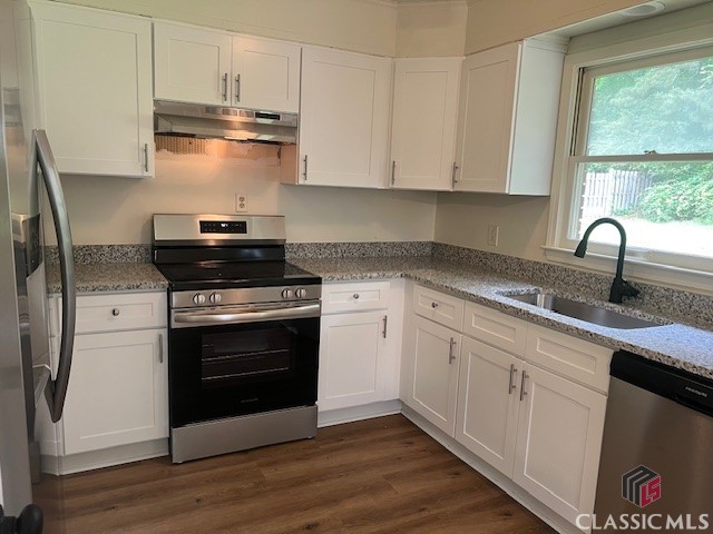 kitchen featuring white cabinets, light stone countertops, a sink, stainless steel appliances, and under cabinet range hood