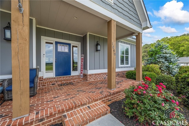 view of exterior entry with board and batten siding, a porch, and brick siding