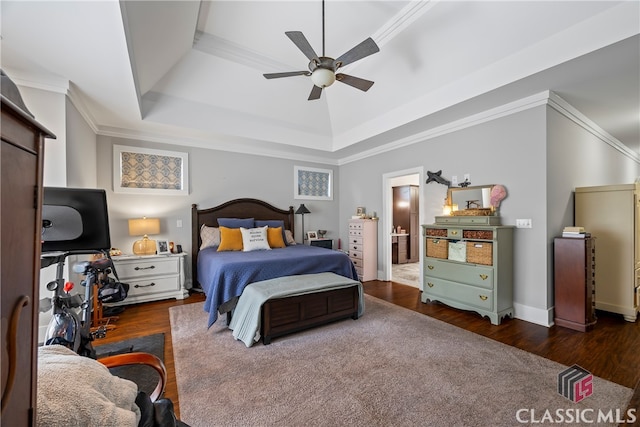 bedroom featuring wood finished floors, crown molding, ensuite bathroom, a raised ceiling, and ceiling fan