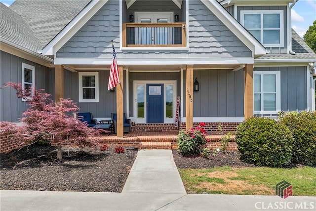 view of exterior entry featuring covered porch, board and batten siding, and a shingled roof