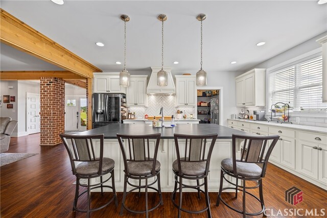 kitchen with a healthy amount of sunlight, stainless steel fridge, custom exhaust hood, and backsplash