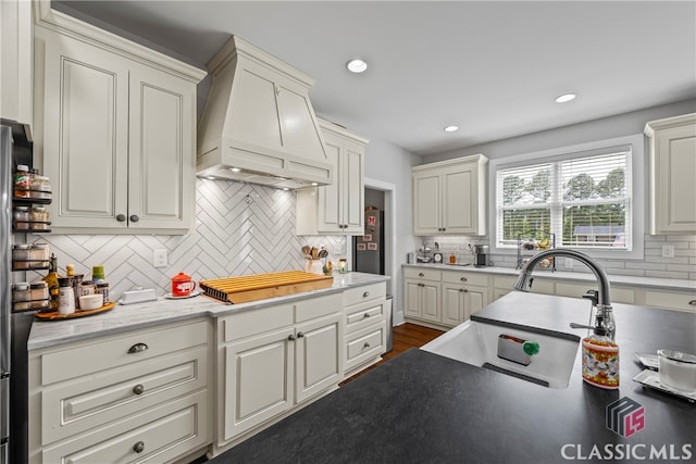 kitchen featuring premium range hood, a sink, recessed lighting, decorative backsplash, and cooktop