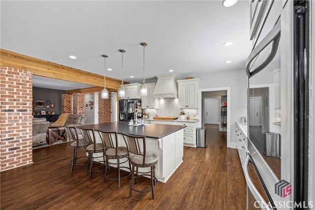 kitchen with a breakfast bar area, dark countertops, open floor plan, stainless steel fridge with ice dispenser, and dark wood-style flooring