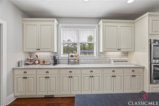 kitchen featuring dark wood-style flooring, stainless steel double oven, light stone countertops, and backsplash