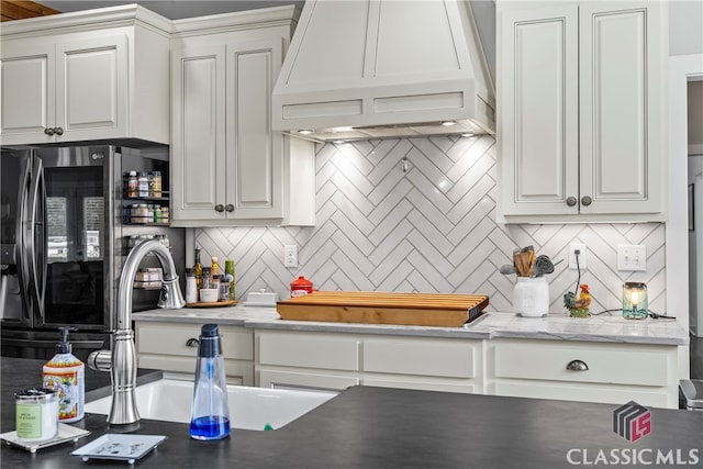 kitchen with backsplash, stainless steel fridge with ice dispenser, premium range hood, and white cabinets