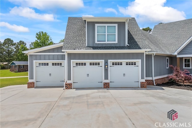 view of front of home featuring board and batten siding, brick siding, a garage, concrete driveway, and roof with shingles