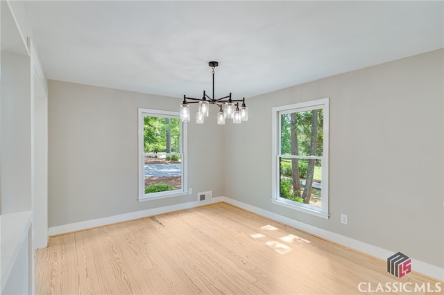 unfurnished room featuring baseboards, light wood finished floors, an inviting chandelier, and visible vents
