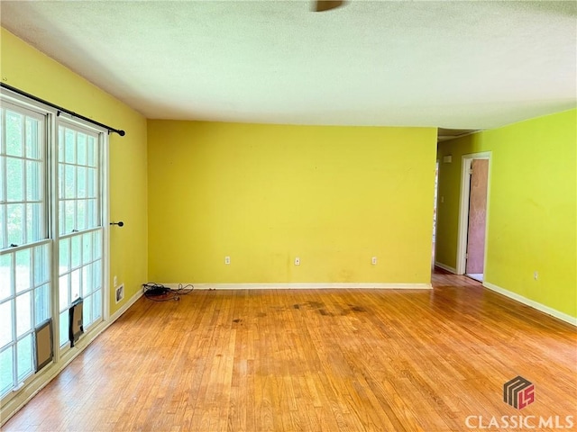 empty room with light wood-style floors, baseboards, and a textured ceiling