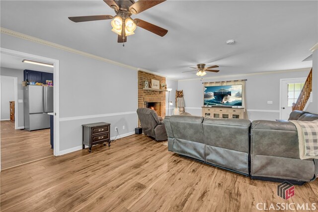 living area featuring a ceiling fan, ornamental molding, a brick fireplace, light wood-style floors, and baseboards