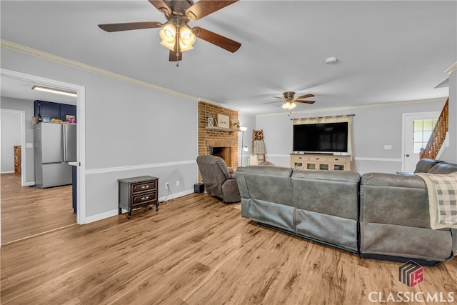 living room with ceiling fan, ornamental molding, a brick fireplace, light wood-style flooring, and baseboards