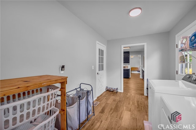 clothes washing area with washer and clothes dryer, light wood-style floors, and baseboards