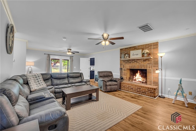 living area featuring ceiling fan, wood finished floors, ornamental molding, a brick fireplace, and baseboards