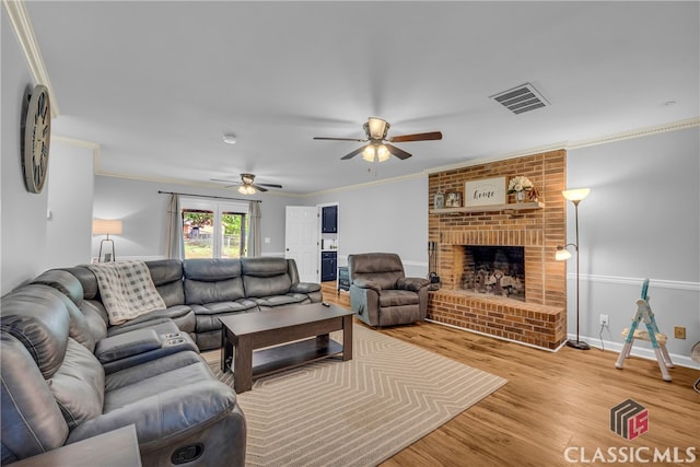 living room featuring a ceiling fan, wood finished floors, crown molding, a fireplace, and baseboards
