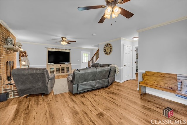 living area with crown molding, ceiling fan, stairs, a fireplace, and light wood-style floors