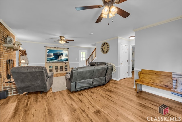 living area with ornamental molding, a ceiling fan, a fireplace, stairway, and light wood finished floors