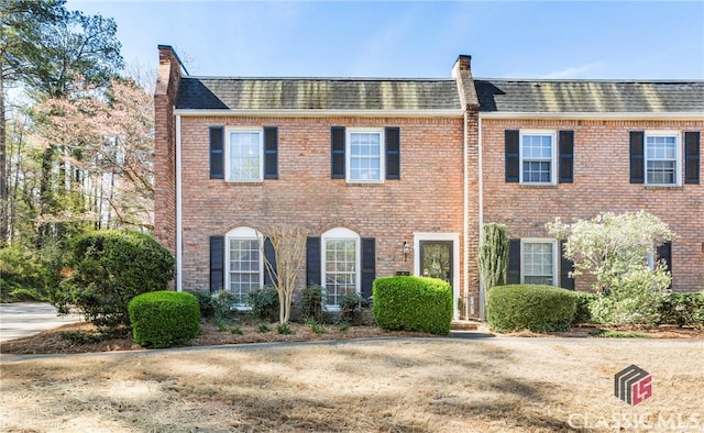view of front of home with a shingled roof, brick siding, and mansard roof