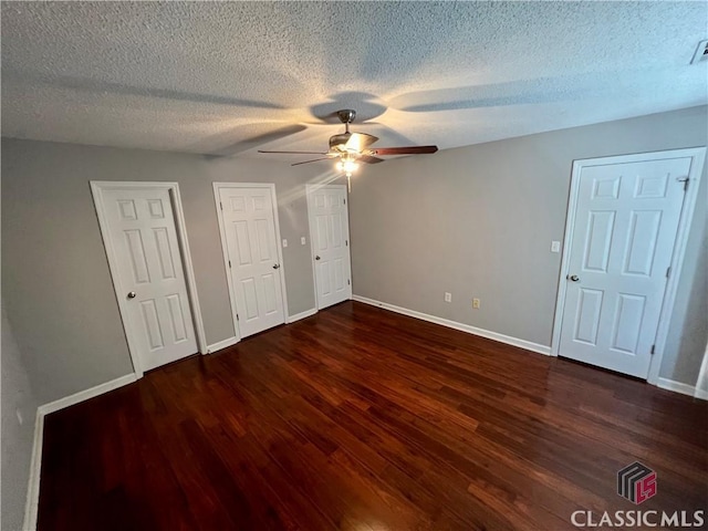 unfurnished bedroom featuring wood finished floors, a textured ceiling, baseboards, multiple closets, and ceiling fan