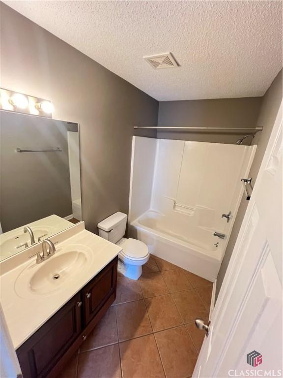 bathroom with vanity, tile patterned floors, a textured ceiling, toilet, and shower / bathtub combination