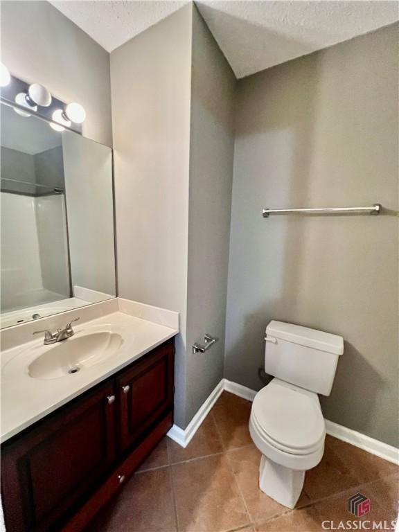 full bathroom with baseboards, tile patterned flooring, toilet, a textured ceiling, and vanity
