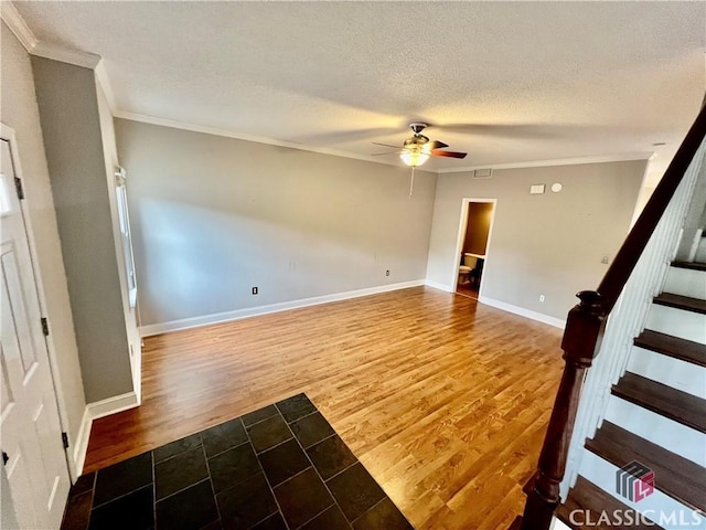 spare room with crown molding, a ceiling fan, a textured ceiling, stairs, and wood finished floors