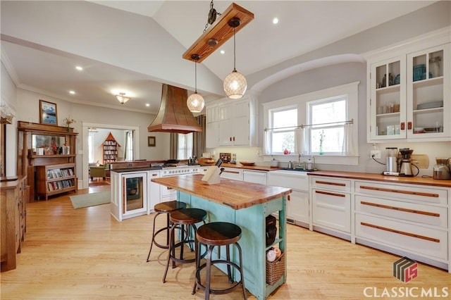 kitchen featuring wooden counters, custom exhaust hood, a sink, white cabinetry, and a kitchen bar