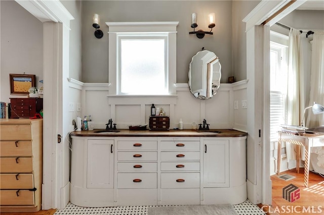 bathroom featuring a decorative wall, a wainscoted wall, double vanity, and wood finished floors