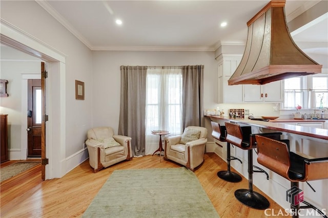 kitchen with crown molding, white cabinetry, light wood-style floors, a kitchen breakfast bar, and island range hood