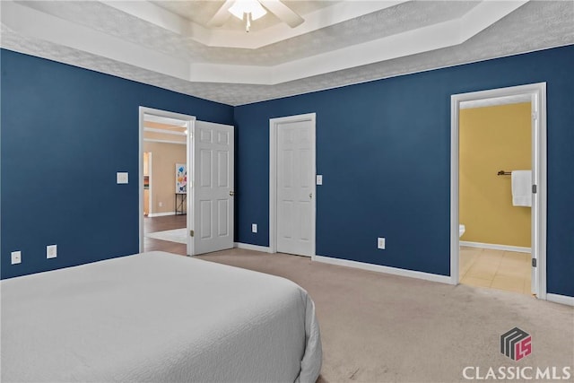 carpeted bedroom with a raised ceiling, baseboards, ensuite bath, and ceiling fan