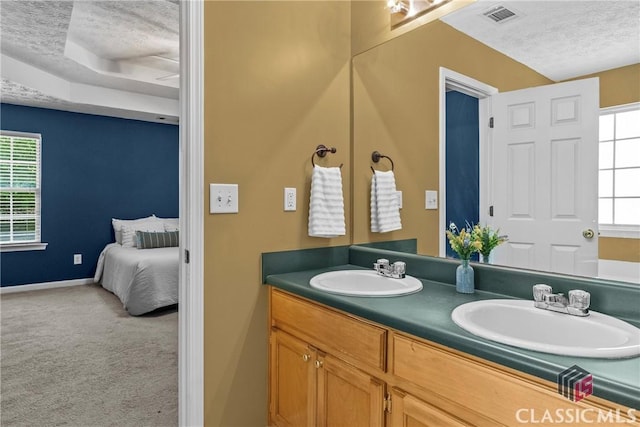 bathroom featuring a textured ceiling, baseboards, double vanity, and a tray ceiling
