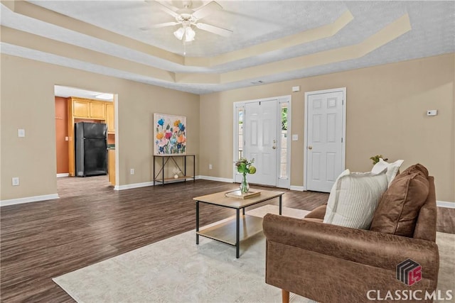 living area with ceiling fan, wood finished floors, baseboards, and a tray ceiling