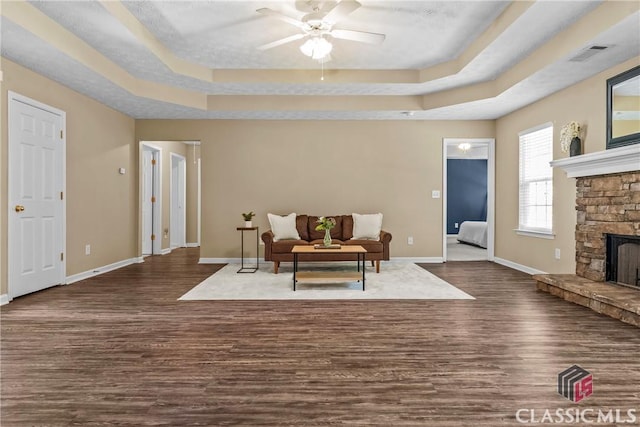 living area with a raised ceiling, dark wood-style flooring, baseboards, and a ceiling fan