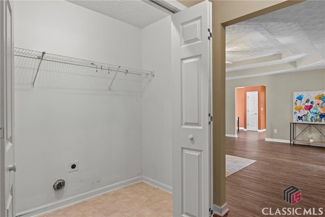 washroom with electric dryer hookup, baseboards, a textured ceiling, and wood finished floors
