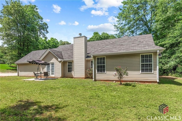 rear view of property with a chimney, a lawn, a patio, and roof with shingles